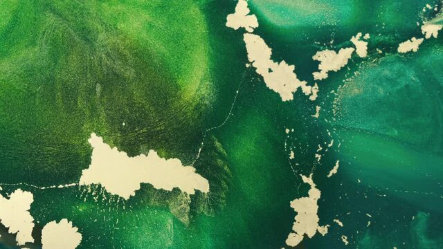 Fluid art, emerald shining wallpaper, close-up. Background of flowing green ink flows in an ocean wave tide, from left side. Liquid texture gold sparkles shimmer in emerald paint. 4k footag abstract