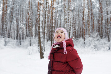 Fototapeta na wymiar a little girl in a red jacket stands in a snow-covered forest. Children's games in the snow-covered forest. Family winter vacation with a child