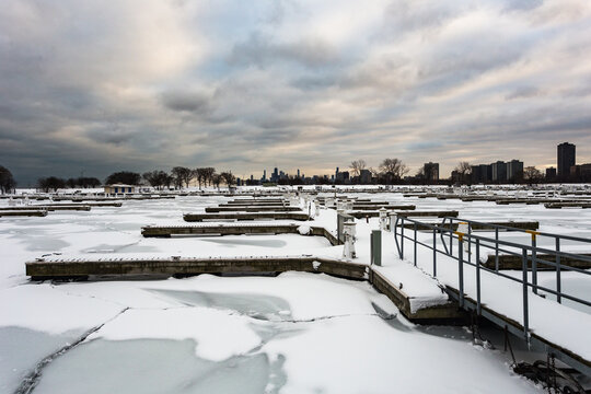 Empty marina with snow covered docks and sheets of ice on cold winter day with overcast sky in urban Chicago