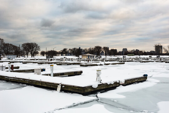 Several snow covered docks sitting in an empty marina with frozen ice sheets on cold winter day with overcast sky in urban Chicago