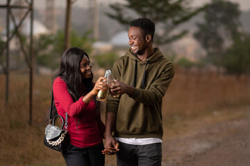 Fototapeta premium young african friends, couple walking and holding hands and having drinks, in happy mood