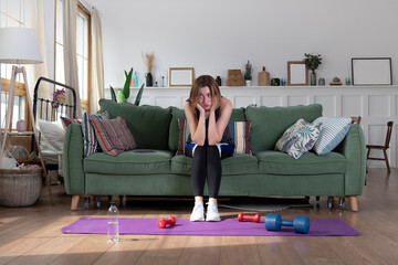 Sad and sleepy girl sitting on the couch and cannot deciding for a morning workout