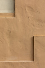 Vertical close-up image of a beige stucco wall, with a small indentation at top left and an...
