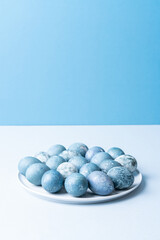 Stylish easter eggs and spring flowers border on blue paper, space for text. Modern natural dyed blue and marble easter eggs. Greeting card template.