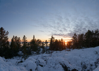 Scenic View on Winter Sunset Over Sea behind forest on coastline, Snowy foreground with very big stones covered by fresh snow, Northern Sweden, Kont, Baltic region.