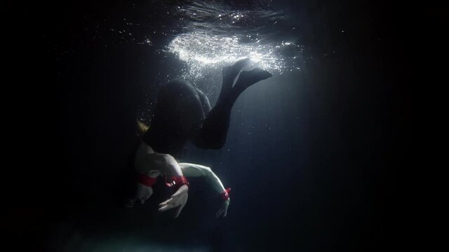 woman dressed in clothes is swimming underwater, diving into dark water