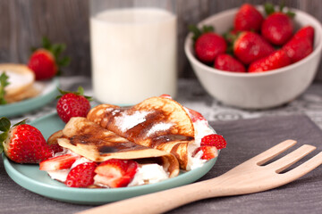 Bodegón de un plato de crepes con nata y fresas, un cuenco de fresas  y una botella de leche en el fondo.