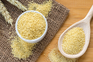 Couscous grains (durum wheat) in wooden spoon and ceramic bowl placed on the bamboo table, top view. Healthy food concept
