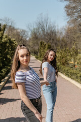 Fototapeta premium Gen z girls enjoying outdoors, expressing positive emotions. Outdoor photo of two girl friends having fun in the park. Two happy joyful young women jumping and laughing together