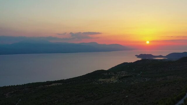 Drone footage of a beautiful sunset at the Gerania mountain in Greece. The drone is facing the sea where the sun is setting, then pan to the right, to see the side of Gerania mountain. 1080p
