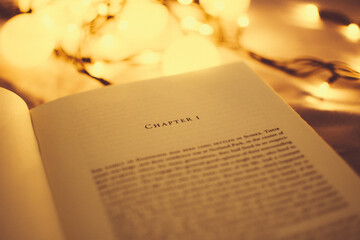 An open book with warm lights focusing on the beginning of it, in chapter one, starting reading