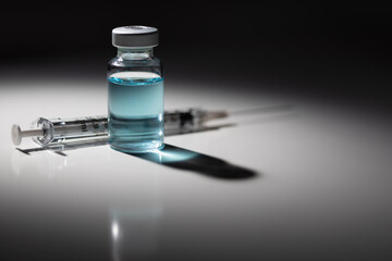 Syringe Needle and Medicine Vial With Light Blue Chemical Spot Lit on Reflective Background