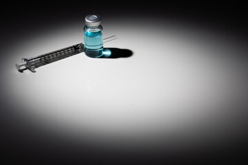 Syringe Needle and Medicine Vial With Light Blue Chemical Spot Lit on Reflective Background