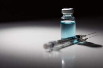 Syringe Needle and Medicine Vial With Light Blue Chemical Spot Lit on Reflective Background