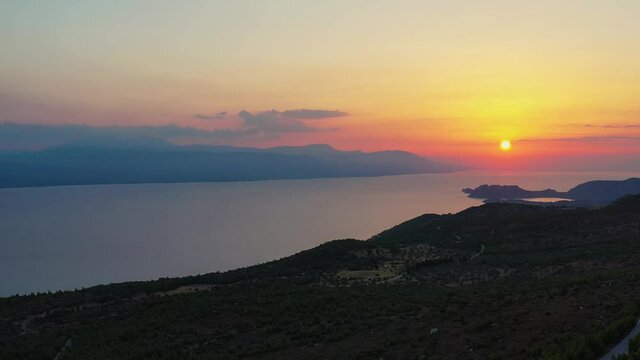 Drone footage of a beautiful sunset at the Gerania mountain in Greece. The drone is facing the sea where the sun is setting, then pan to the right, to see the side of Gerania mountain. 4K