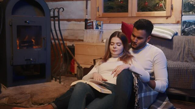 Happy young couple relaxing and reading book together near the fireplace. Winter holidays, christmas or valentines day. High quality 4k footage