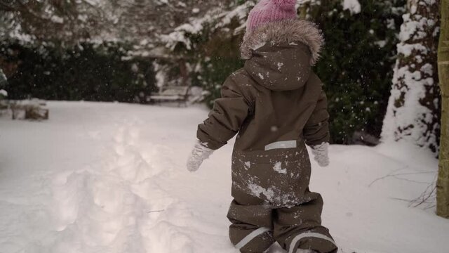 Child walking in snowy garden when snowing in slow motion