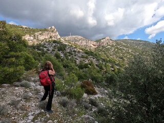 Naklejka na ściany i meble Woman hiker with red backpack photographing mountain scenery in Greece