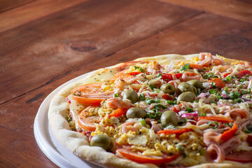 pizza with ham, cheese, tomato, egg and olives on rustic wooden table.