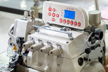 Close-up of details of modern white professional electric sewing machine with electronic control panel on a table in factory. Work place of seamstress. No People.