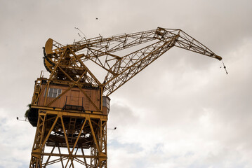 A yellow harbor crane. Bottom view of a large crane against cloudy sky.