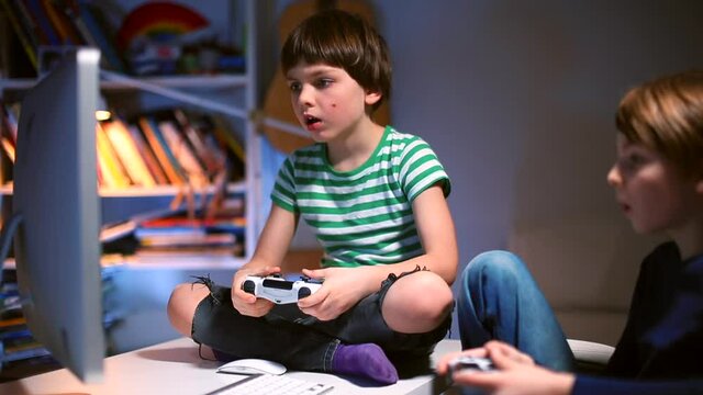 A teenager boy vigorously plays on the controller in his hands while sitting on the table. Emotions on the face of a playing person ps4. Emotional relaxation at your leisure.