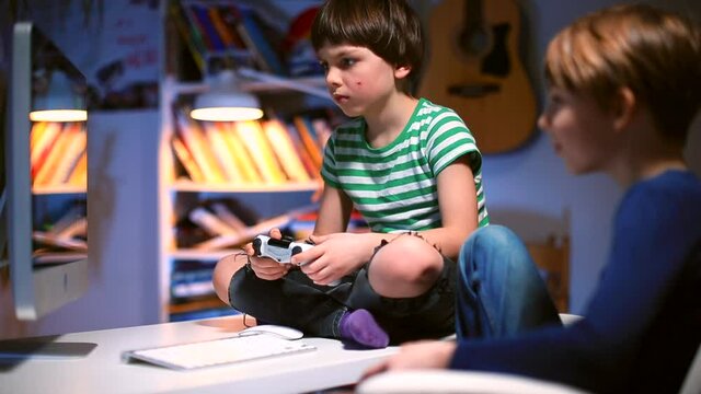 Two tired teenagers stare at the monitor at the end of the day. Evening room. Focus of attention in the monitor screen. Emotional relief ps4.