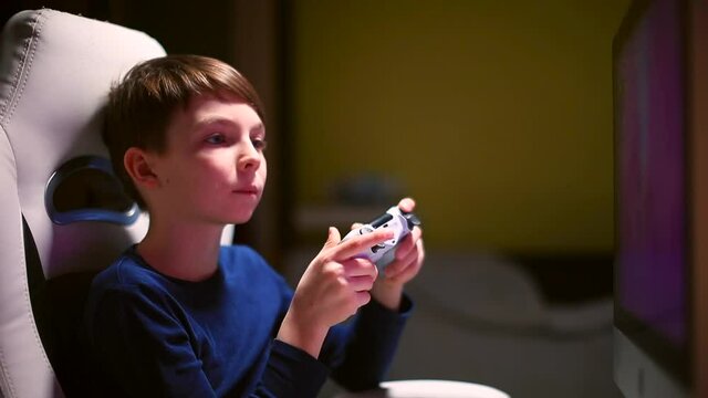 Smart boy is playing a video game using a monitor. Hold the game controller in your hands, shows the gesture of success. Emotions in a video game ps4.