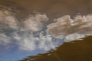 Abstract painterly image of clouds reflected in wet sand at a beach