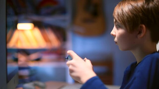 The teenager looks at the monitor screen. Play an electronic game ps4. Victory gesture, next level. Motivation of the child's positive emotions. Spending free time at home in the evening.