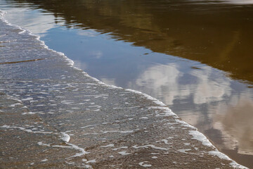Abstract painterly image of clouds reflected in wet sand at a beach