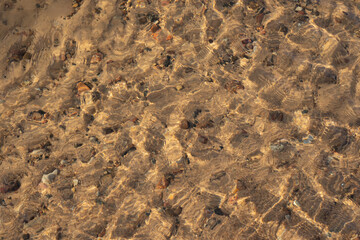 the water swirls and forms a texture through which you can see yellow sand and small stones