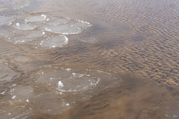the water swirls and forms a texture through which you can see yellow sand and small stones