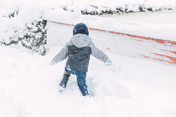 Fototapeta na wymiar Boy walking in knee-deep snow with colorful winter clothes and covid mask 