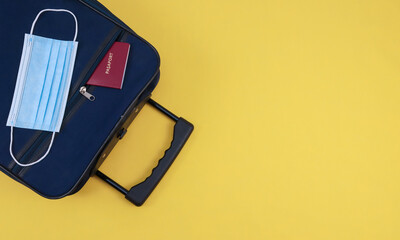 Suitcase on yellow.

Blue suitcase with a passport and a mask on the left on a yellow background with a place for text on the right, top view close-up.