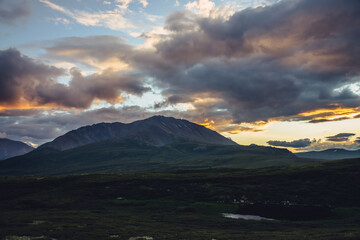 Beautiful mountain scenery with golden dawn light in cloudy sky. Scenic mountain landscape with illuminating color in sunset sky. Silhouettes of mountains on sunrise. Gold illuminating sunlight in sky