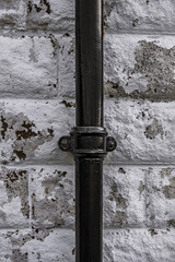 Old black cast iron vertical drain pipe affixed to an old white stone wall shot straight on.