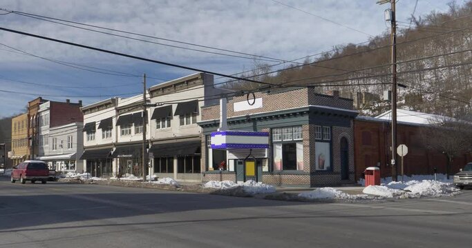 A daytime winter establishing shot of typical businesses along the main street of a small Appalachian town. A movie theater seen on the corner.  	