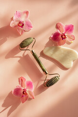 Obraz na płótnie Canvas Facial massage roller jade on a pink background. Morning facial treatments for beauty. Pink orchids. Relax on the weekend at the spa.