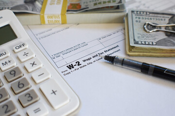 W-2 Employee IRS Tax Form For Yearly Earnings From An Employer With Calculator, Money And Pen Close Up