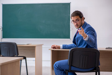 Young male teacher in suit in front of green board