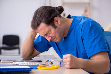 Young male sick doctor being unhappy after night shift