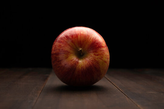 still life image of one organic gala apple close up on rustic wooden surface and black background