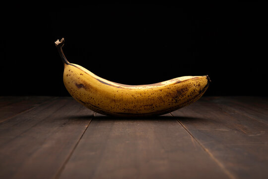 image of ripe yellow banana close up on rustic wooden surface and black background
