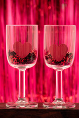 Two wineglasses with little red stars and hearts on red and pink background. Valentine's Day decoration