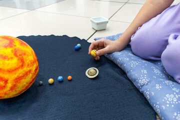 Top view of girl's hand holding planet on dark background at Montessori school.