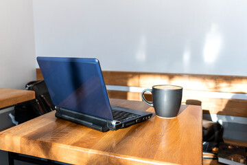 Black cup with coffee stands on a wooden table next to a laptop.