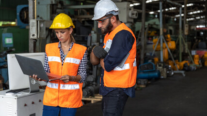 Male and female mechanical engineers or factory workers with safety gears and hard hats discuss about production project using computer laptop to plan in a warehouse