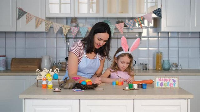 Little Girl with Mother Preparing Easter Decorations in the Kitchen. Cute Little Rabbit is Sitting on the Foreground. Spring Season, Family, Easter Holiday Preparation and People Concept