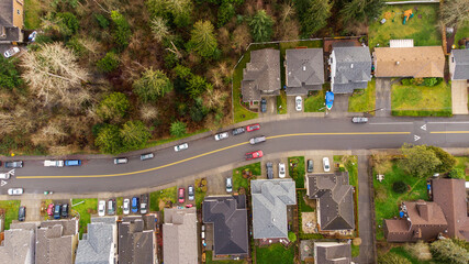 Aerial view of residential neighborhood surrounded by trees. A small road divides houses as cars...